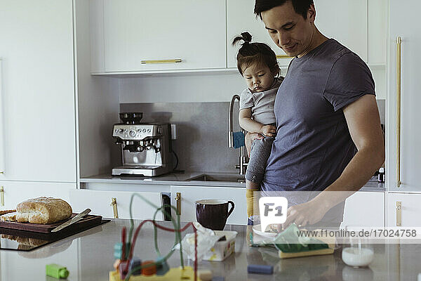 Father with food carrying male toddler by kitchen counter