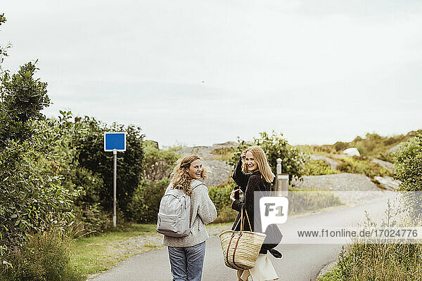 Lächelnde weibliche Freunde schauen über die Schulter beim Gehen auf der Straße während des Sommerurlaubs
