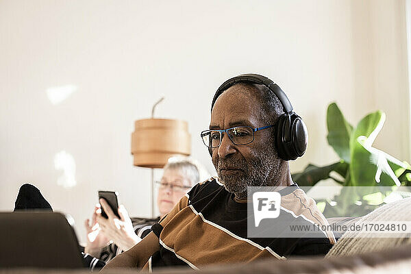 Älterer Mann mit Kopfhörern  der einen Laptop zu Hause benutzt