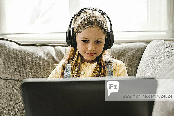 Vorpubertäres Mädchen konzentriert sich beim E-Learning am Laptop im Wohnzimmer