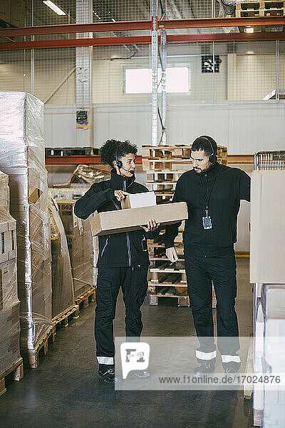 Weibliche Unternehmerin hält Pakete  während sie sich mit einem männlichen Kollegen im Logistiklager unterhält