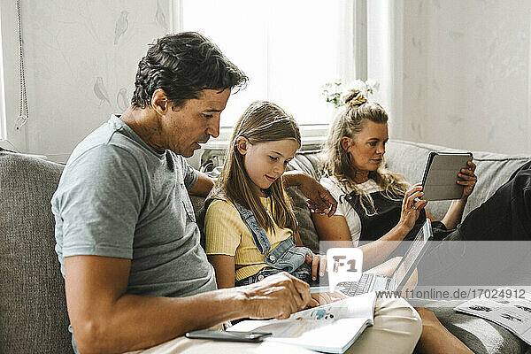 Vater unterrichtet Tochter  während die Mutter daneben sitzt und ein digitales Tablet zu Hause benutzt