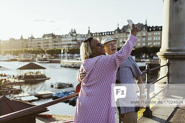 Lächelnde ältere Paar unter selfie während stehend auf Brücke gegen See in der Stadt