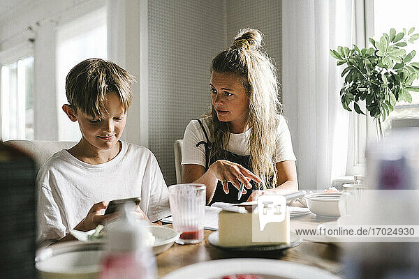 Mutter unterrichtet  während Sohn Smartphone zu Hause benutzt