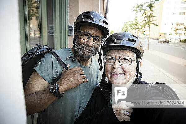 Lächelndes älteres Paar nimmt Selfie mit Fahrradhelm vor dem Haus