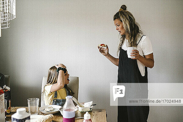 Tochter weigert sich  Frühstück zu essen  während Mutter mit Kaffeetasse zu Hause steht