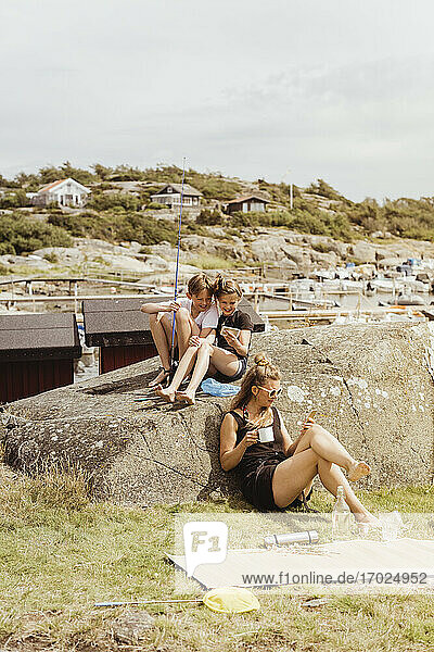 Siblings and mother using mobile phone while sitting at marina