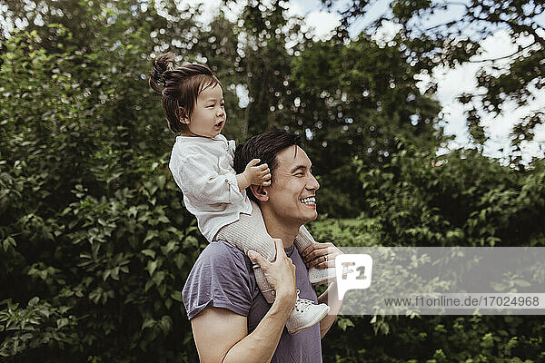 Glücklicher Vater trägt Baby Sohn auf der Schulter durch Bäume im Park