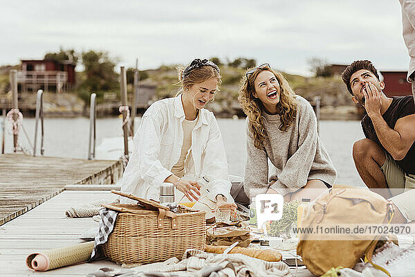 Friends laughing while having snacks during picnic at harbor