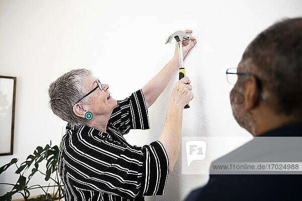 Lächelnde Frau hämmert Nagel an der Wand  während er von älteren Mann zu Hause