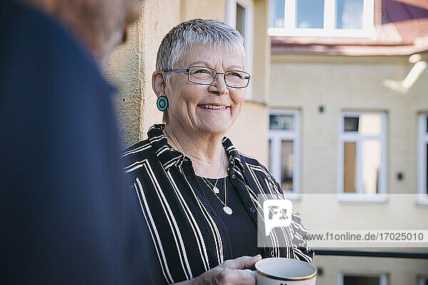 Lächelnde Frau mit Kaffeetasse von Mann in Balkon