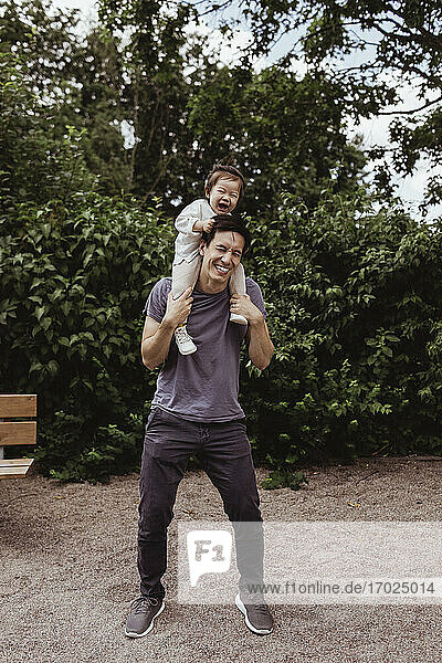 Fröhlicher Vater trägt Sohn auf Schulter in Spielplatz