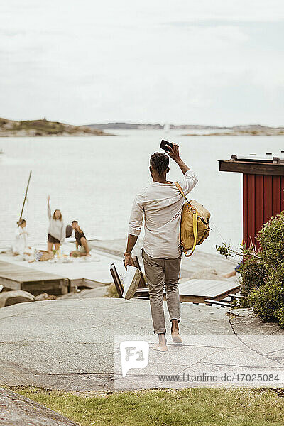 Rückansicht eines Mannes  der seinen Freunden beim Picknick am Hafen auf dem Steg zuwinkt