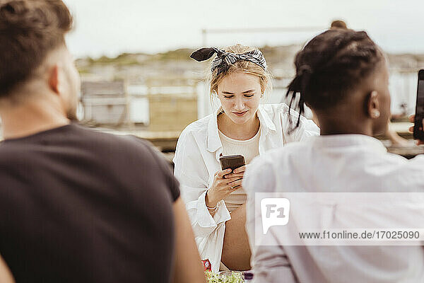 Lächelnde Frau verwendet Smartphone mit Freunden beim Picknick