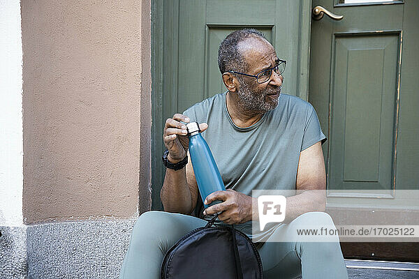 Älterer Mann mit Flasche  der wegschaut  während er gegen den Türrahmen sitzt