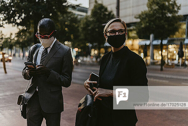 Männliche und weibliche Kollegen stehen mit Smartphone auf dem Fußweg während der Pandemie