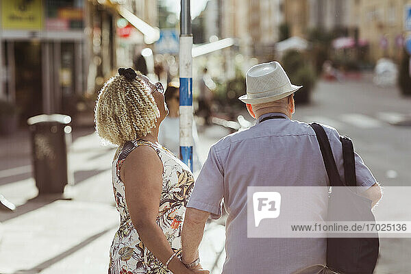 Senior woman holding hand on man while walking in city during sunny day