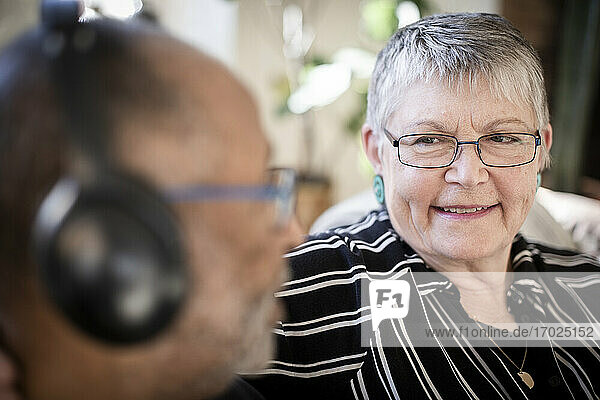 Lächelnde Frau schaut Mann mit Kopfhörer zu Hause an
