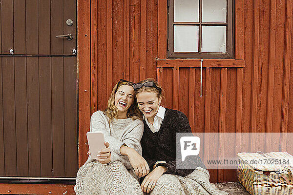 Weibliche Freunde lachen  während sie Selfie auf Handy gegen Hütte