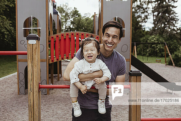 Smiling father and son leaning over monkey bar in park