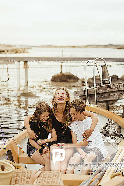 Lächelnde Mutter mit Armen um Kinder sitzen in Boot am Yachthafen