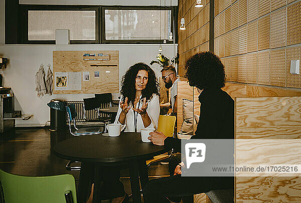 Geschäftsfrau diskutiert mit männlichen Kollegen im Büro während der Kaffeepause