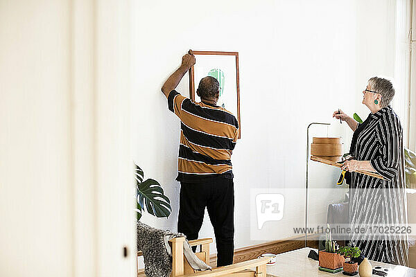 Älterer Mann justiert Gemälde  während er gegen Frau im Wohnzimmer steht