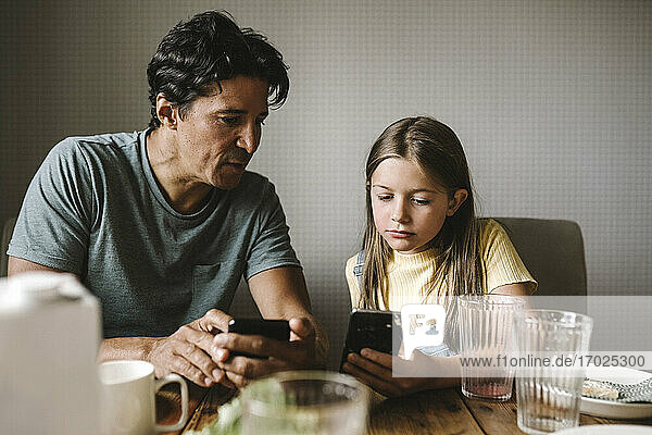 Tochter und Vater mit Smartphone über Esstisch zu Hause
