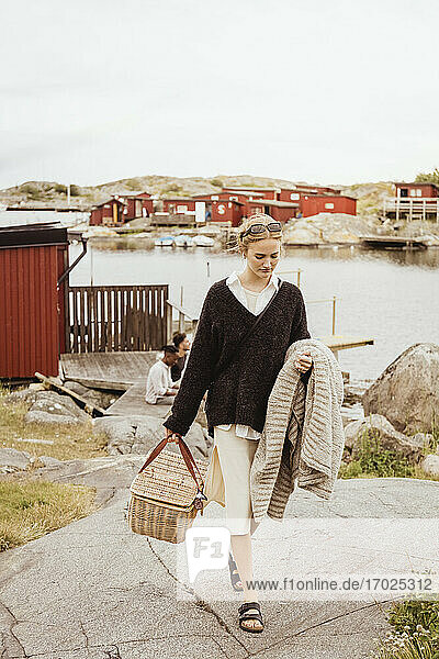 Junge Frau zu Fuß mit Picknickkorb und Decke gegen den Hafen