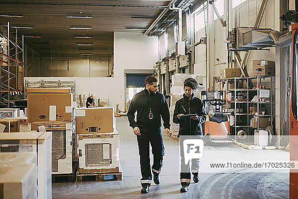 Female and male colleagues discussing over digital tablet while walking in warehouse