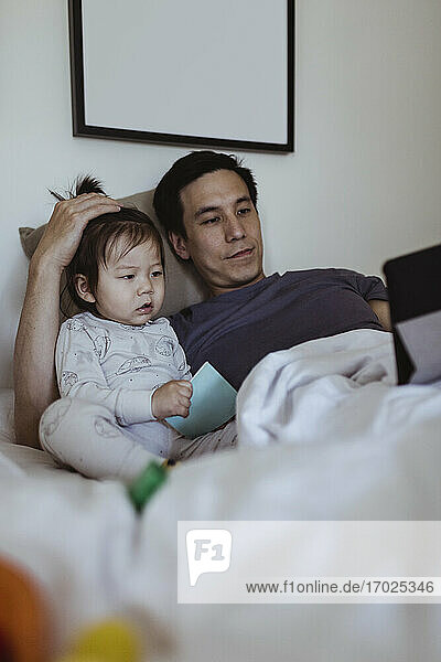 Vater benutzt digitales Tablet von männlichem Kleinkind im Schlafzimmer