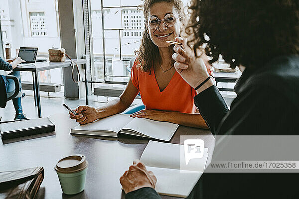 Smiling businesswoman discussing with male colleague at coworking office