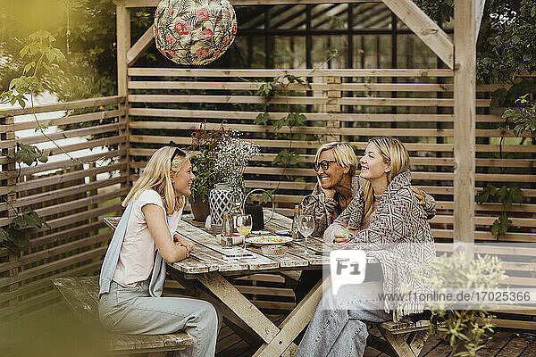 Lächelnde Freundinnen verbringen Zeit mit Großmutter am Tisch im Vorgarten