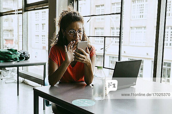Geschäftsfrau mit Smartphone beim Sitzen am Schreibtisch im Büro