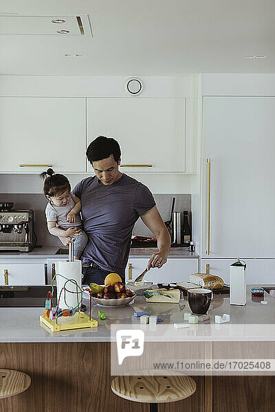 Father carrying baby son while preparing food in kitchen