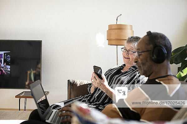 Frau mit Smartphone sitzt neben Mann mit Laptop zu Hause