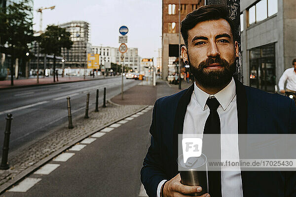 Porträt eines Geschäftsmannes mit isoliertem Getränkebehälter auf dem Fußweg stehend