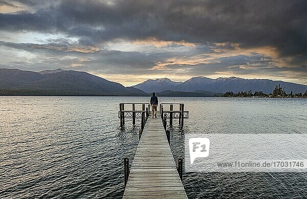 Juger Mann auf Steg am See  Lake Te Anau bei Sonnenuntergang  Te Anau  Südinsel  Neuseeland  Ozeanien