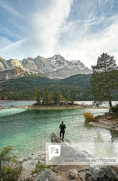 Young woman standing on a rock on the shore  view into the distance  Eibsee lake in front of Zugspitzmassiv with Zugspitze  Wetterstein range  near Grainau  Upper Bavaria  Bavaria  Germany  Europe