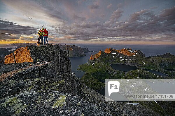 Zwei Wanderer am Gipfel  Sonnenuntergang mit dramatischen Wolken  Ausblick vom Gipfel des Hermannsdalstinden  Fjorde  Seen und Berge  Moskenesøya  Lofoten  Nordland  Norwegen  Europa