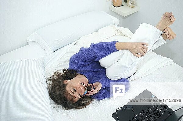 Woman having breakfast and working with her computer in bed while talking to her phone