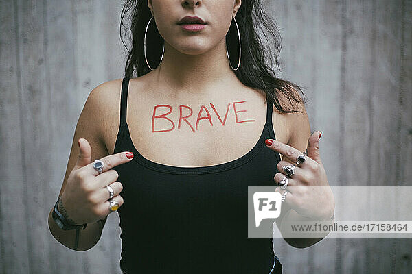 Midsection von weiblichen Protestler zeigt auf mutigen Text über Brust gegen Wand geschrieben