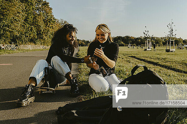 Lächelnde weibliche Freunde mit Smartphone sitzen im Park