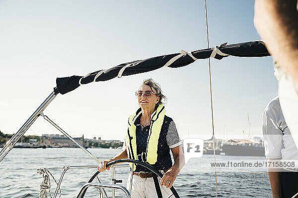 Aktive ältere Frau Segelboot mit Freunden gegen klaren Himmel an einem sonnigen Tag