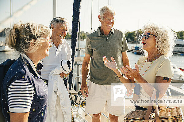 Smiling senior couples talking with each other on boat during sunny day