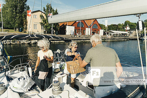 Weibliche und männliche Freunde mit Picknick Dinge in Segelboot auf sonnigen Tag