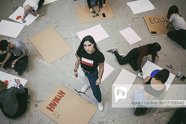 Hochwinkliges Porträt einer stehenden Frau  während ein männlicher und ein weiblicher Aktivist Schilder in einem Gebäude vorbereiten
