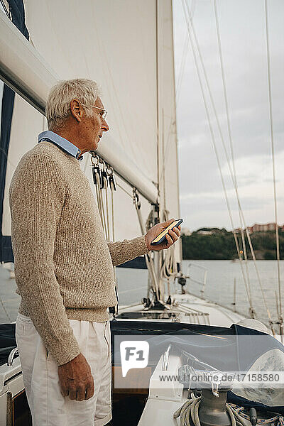 Älterer Mann navigiert Richtung durch Smartphone  während er auf einem Boot während des Sonnenuntergangs steht