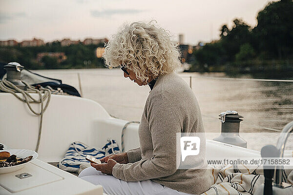 Senior Frau Text-Messaging auf Smartphone  während in Boot während des Sonnenuntergangs sitzen