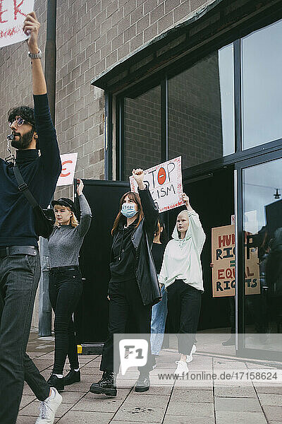 Junger Mann und junge Frau protestieren mit Stop Racism vor dem Gebäude während der Pandemie